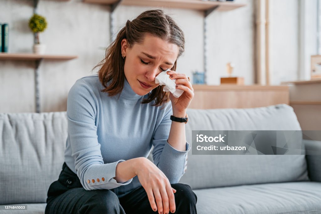 Young Woman Crying Beautiful young woman sitting on the sofa in the living room and crying. Crying Stock Photo