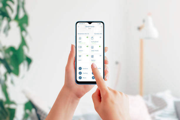 istock Control home devices with smart home app. Smart phone in hands, living room interior in background. Modern home automation app interface 1374843748