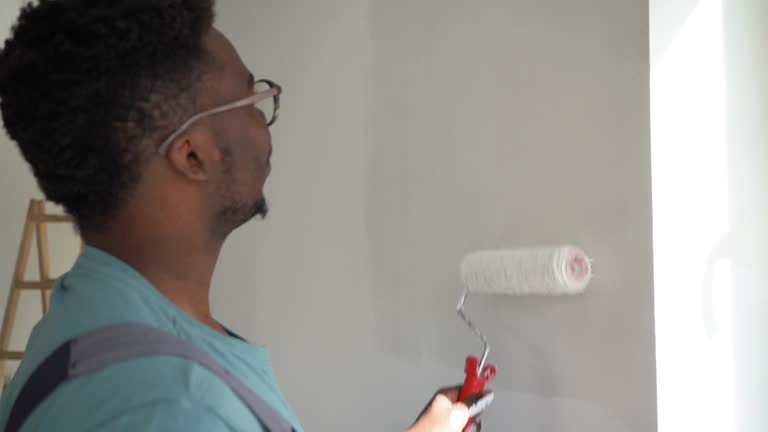 African-American professional painter paints the wall indoors