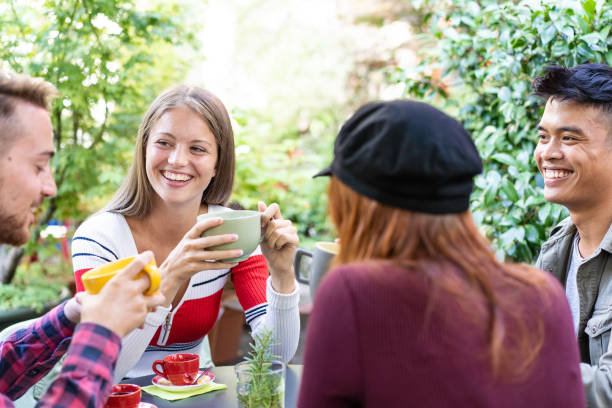 Young people drinking cappuccino and espresso coffee at cafe bar garden - Happy friends talking and having fun together at hostel dehors - Lifestyle concept with happy guys and girl at open-air cafe