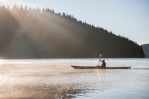 Active senior man kayaking in mountain lake on sunrise.
