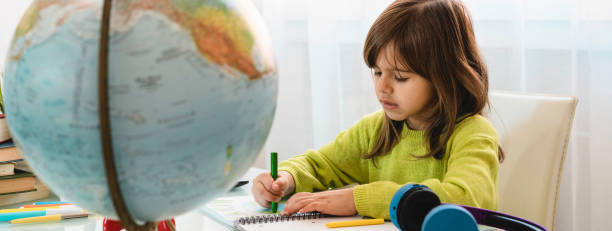 istock Horizontal banner or header with cute child girl doing homework at home - Pre or elementary schooler girl drawing and painting the world on the school notebook with wax colors 1374877402