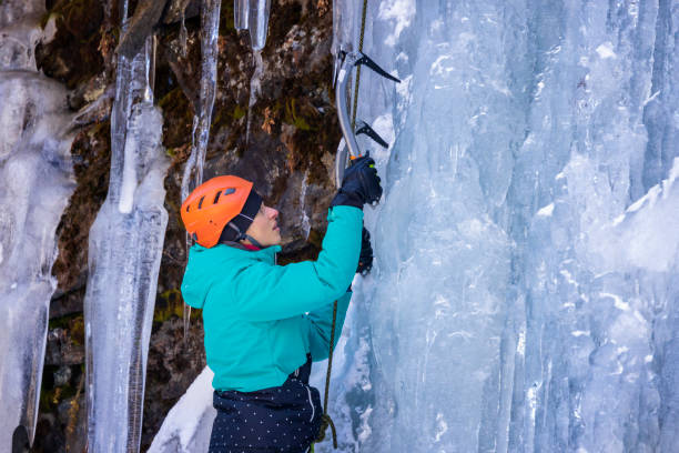 Young woman climbing a frozen waterfall with ice climbing gear