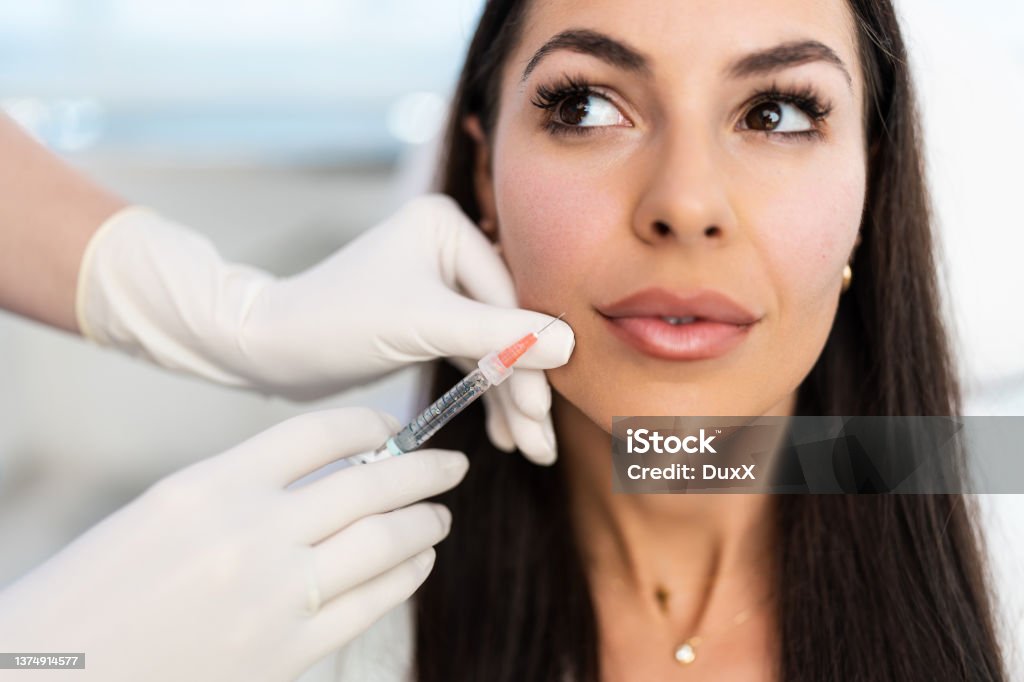 Modern beauty treatment Attractive woman is getting a rejuvenating facial injections at beauty clinic. The expert beautician is filling female wrinkles with botulinum toxin injections or hyaluronic acid fillers. Dermal Filler Stock Photo