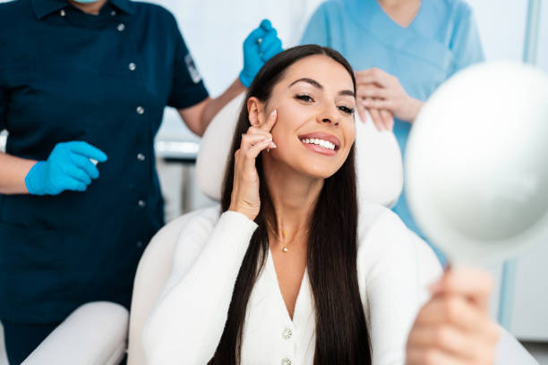 Beautiful young woman at beauty clinic Beautiful and happy young woman sitting in medical chair and looking in the mirror. She is satisfied after successful beauty treatment with hyaluronic acid fillers or botulinum toxin injections. beauty treatments stock pictures, royalty-free photos & images