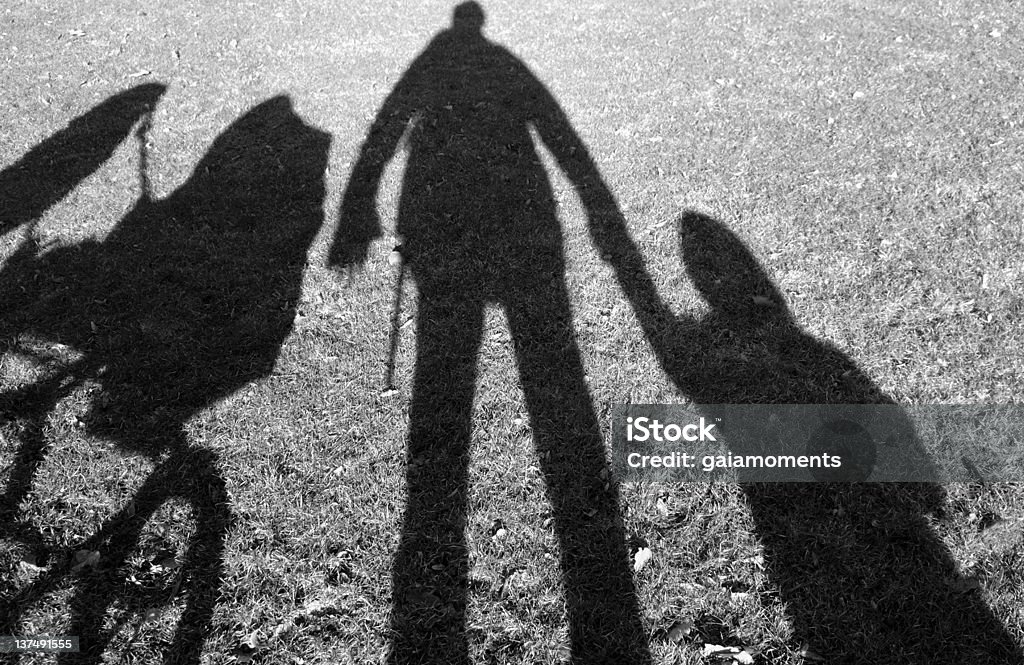Shadows of person holding hands with a baby and a stroller Shadow on lawn of a father, a small child and a baby carriage. Kidnapping Stock Photo