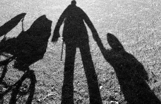 Shadow on lawn of a father, a small child and a baby carriage.