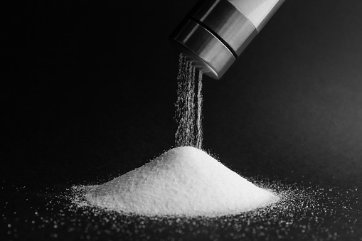 Pouring salt from shaker on black background, closeup