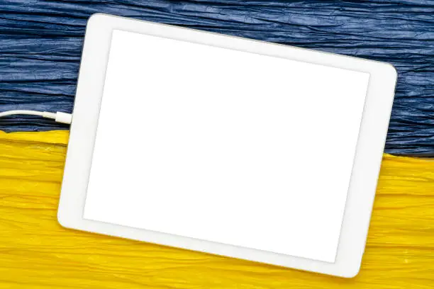 mockup of digital tablet with a blank isolated screen (clipping path included) against paper abstract in colors of Ukraine national flag, blue and yellow