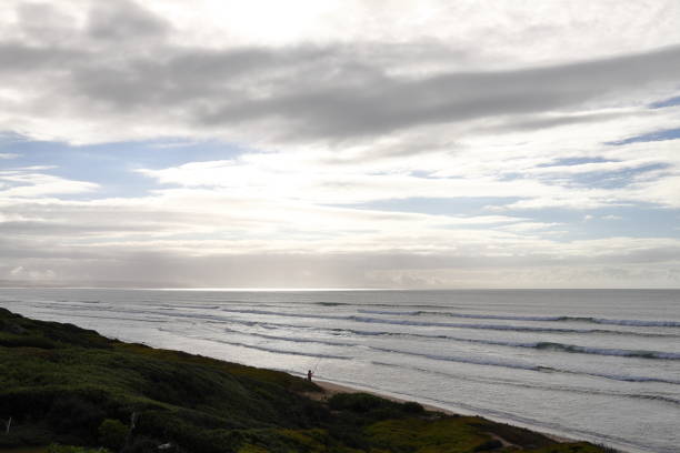 A view over the ocean towards the sun which is obscured by clouds.