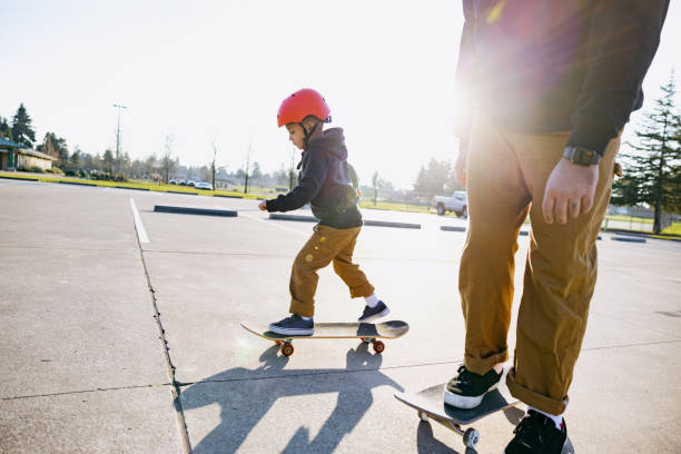 A Hispanic dad rides a skateboard with his 5 year old child, enjoying the time together.
