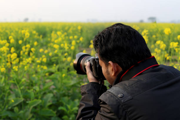 professional photographer in rain clothes with professional camera and telephoto lens outdoors in dry grass looking at camera
