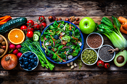Overhead view of a blue plate with healthy salad shot on rustic wooden table. Multi colored fresh fruits, vegetables, seeds and nuts are around the salad plate. High resolution 42Mp studio digital capture taken with SONY A7rII and Zeiss Batis 40mm F2.0 CF lens