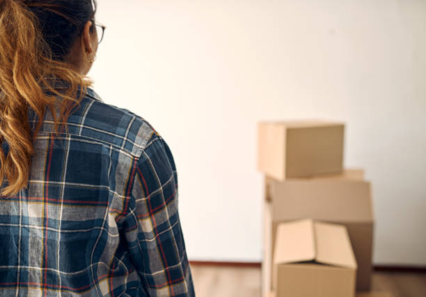 Rearview shot of a woman looking at boxes in an empty room stock photo
