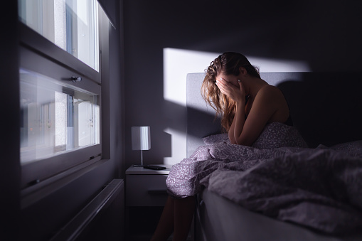 Sad depressed woman in bed. Lonely person with stress, insomnia and trouble sleeping. Anxiety, sorrow, solitude, grief or panic. Restless tired and desperate girl crying with emotion.