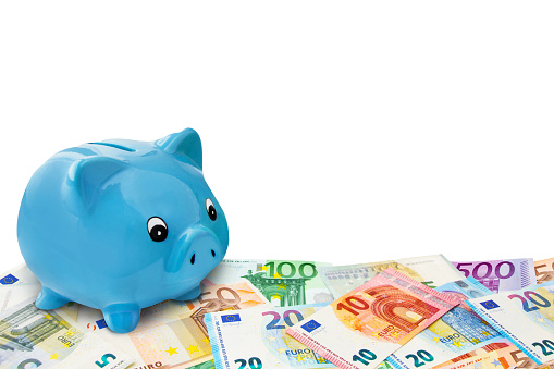 Finances and symbolic blue Piggy Bank with Euro banknotes isolated against white background