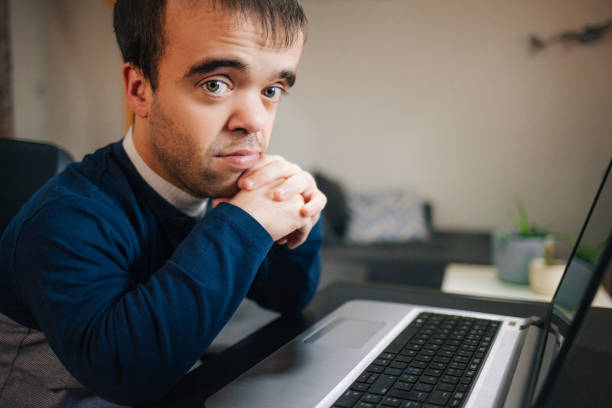 Thoughtful businessman or manager in the office sitting behind a laptop with his chin on his hands staring ahead with a contemplative expression
