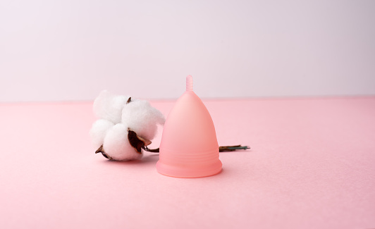 Una copa menstrual y una ramita de algodón sobre un fondo de rosa. photo