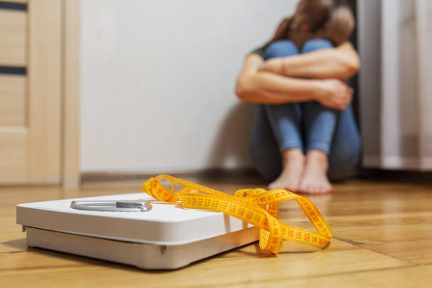 White scale and depression, upset and sad woman with measuring tape on wooden floor White scale and depression, upset and sad woman with measuring tape on wooden floor. anorexia nervosa stock pictures, royalty-free photos & images