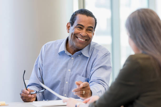 Mature doctor smiles while discussing documents with female administrator stock photo