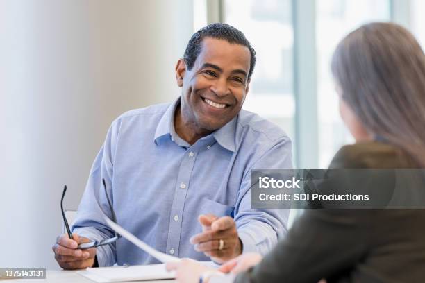 Mature Doctor Smiles While Discussing Documents With Female Administrator Stock Photo - Download Image Now