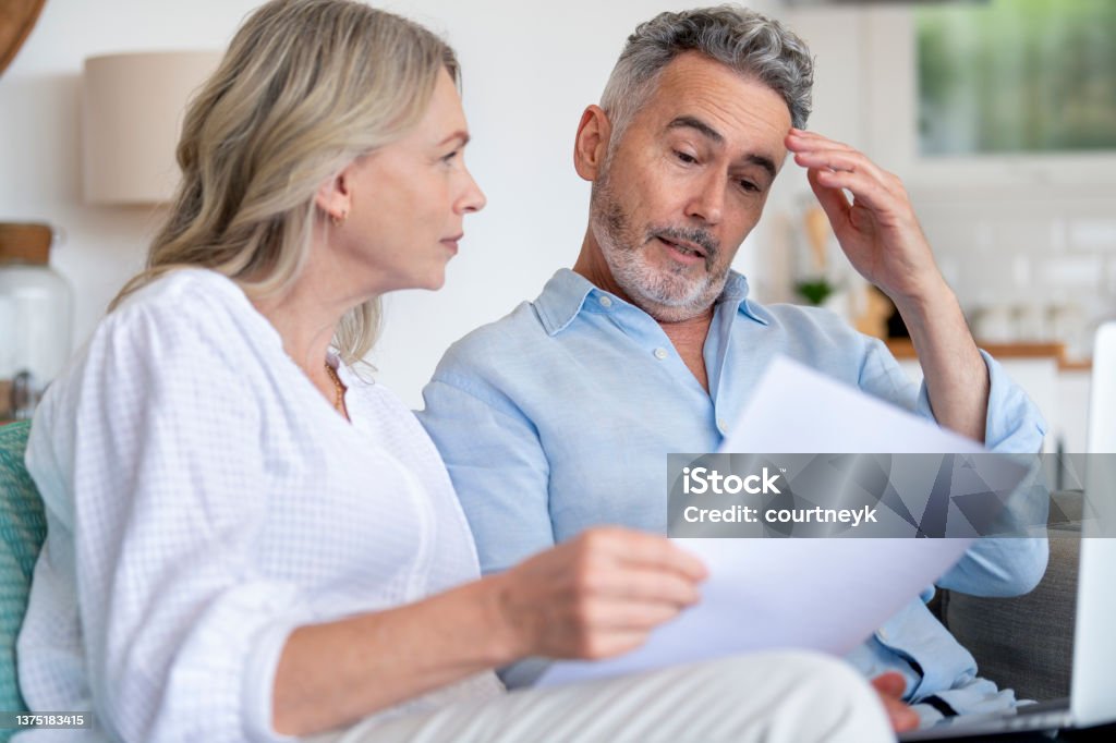 Mature couple doing paperwork with a laptop at home. Mature couple doing paperwork with a laptop at home. They look concerned, shocked and worried Financial Bill Stock Photo