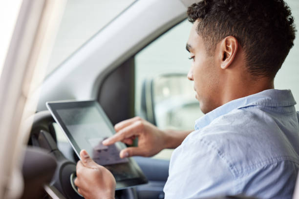 shot of a young delivery man using a digital tablet while sitting in a van - postal worker truck driver delivering delivery person imagens e fotografias de stock