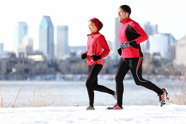 Runners running in winter snow with city background. Healthy multiracial young couple woman and man Montreal skyline, Quebec Canada