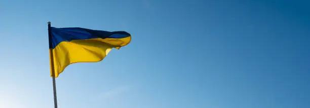 Flag of Ukraine on blue sky background. National symbol of freedom and independence. "Slava Ukraini!" (Glory to Ukraine).