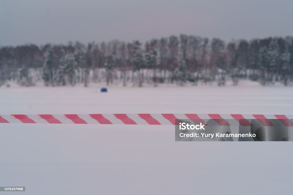 Red and white barrier tape in front of frosen river Photography of closed way. The passage is closed. Red and white barrier tape.  It 's getting warmer outdoors due to spring coming. The ice on the river has become thin, you can't walk on it Abstract Stock Photo