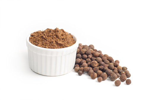 Allspice whole ,beside ground allspice in small white bowl isolated on white background