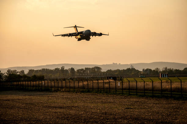 A large military cargo plane lands at an orange sunset at Brno Airport in the Czech Republic