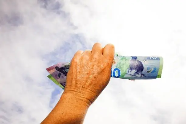 A human fist is held in the air holding New Zealand Dollars Money (NZD). This is a Concept Image.