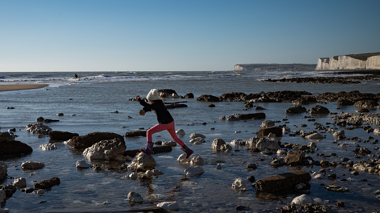 A young girl jumps across rocks on the beach at Birling Gap in the South Downs, East Sussex, UK