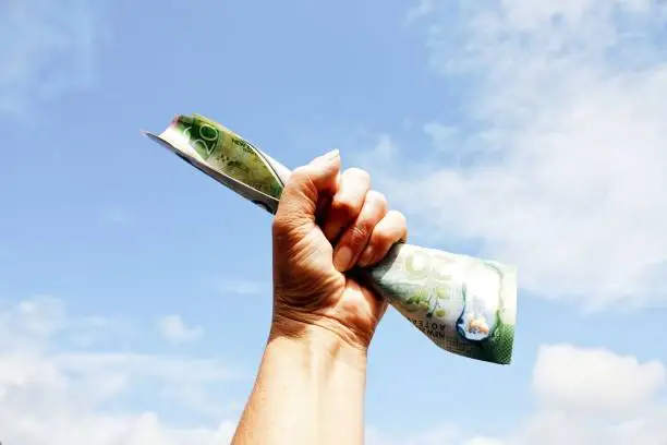 A human fist is held in the air holding New Zealand Dollars Money (NZD). This is a Concept Image.