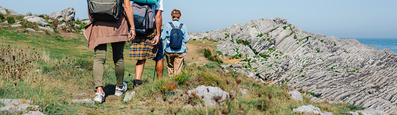 Unrecognizable senior couple with their adult daughter on their backs trekking in family