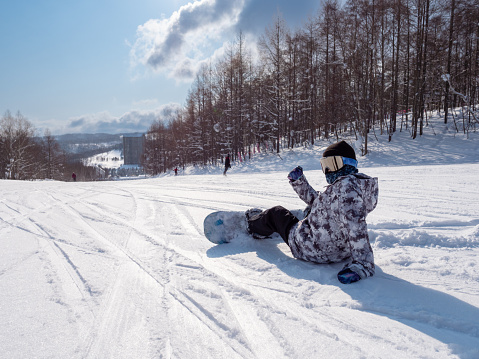 Teenage girl visiting Hokkaido in winter and enjoying snowboarding.