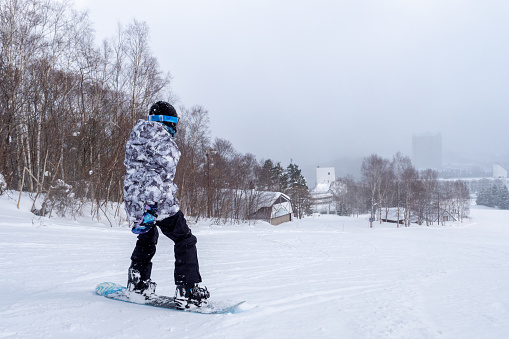 Teenage girl visiting Hokkaido in winter and enjoying snowboarding.