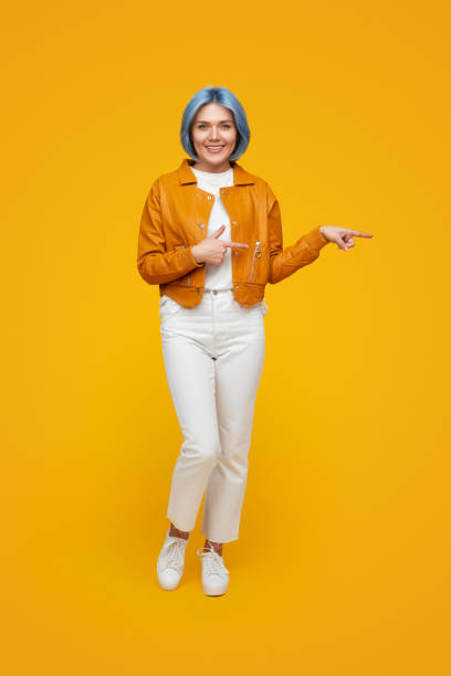 istock Cheerful young woman pointing away while standing in yellow studio 1375438870