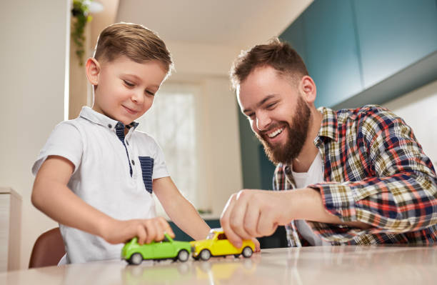 Cheerful father and son playing with toy cars Happy loving dad enjoying time with little son and playing with toy cars during weekend at home kid toy car stock pictures, royalty-free photos & images