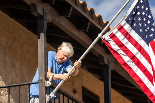 High quality stock photo of a senior veteran hanging an American flag outside his home.