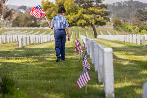 High quality stock photos of a young boy placing American flags on veterans graves at a veterans cemetery on Memorial Day.