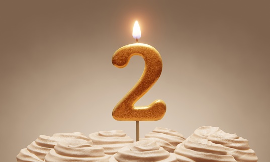 2nd birthday or anniversary celebration. Lit golden number candle on cake with icing in neutral tones. 3D rendering