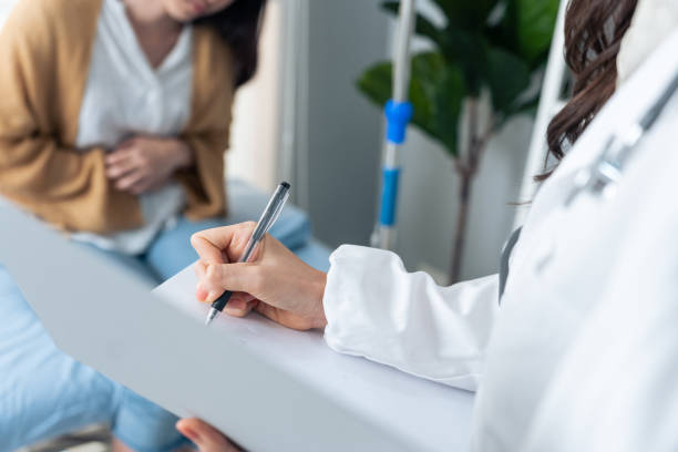 mulher asiática paciente visitar e consultar problema de saúde com jovem médico. menina doente se sente magoada e dolorosa sofrendo de dor de estômago e depois explica para terapeuta atraente no hospital de escritório - abdómen - fotografias e filmes do acervo