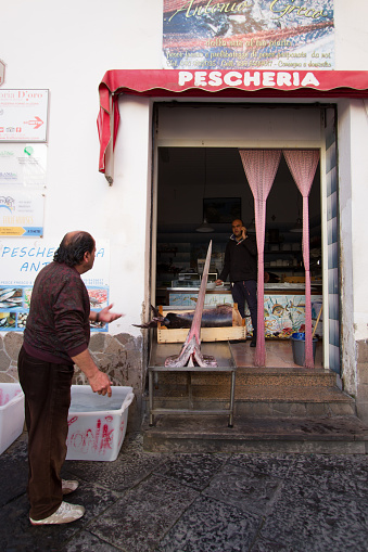 Lipari, Aeolian Islands, Sicily, Italy: Two fishmongers talking outside a small fish shop (pescheria) in downtown Lipari.