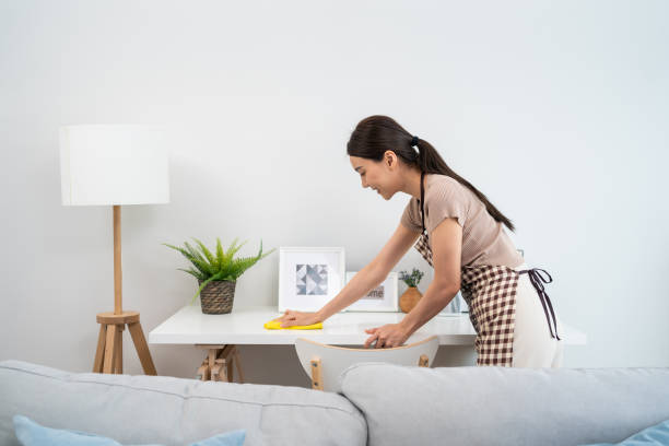 Asian cleaning service woman worker cleaning in living room at home. Beautiful girl housewife housekeeper cleaner feel happy and wiping messy dirty working table for housekeeping housework or chores. stock photo