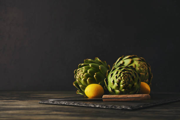 Still life with artichokes and lemons on a slate cutting board with a kitchen knife
