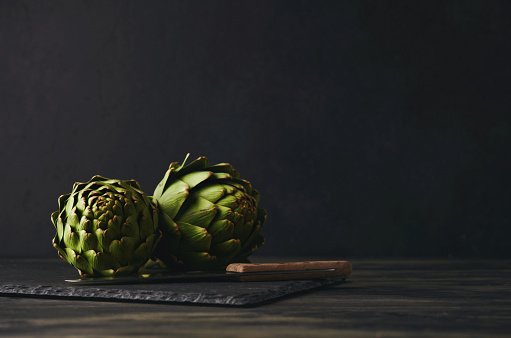 Still life with artichokes on a slate cutting board with a kitchen knife