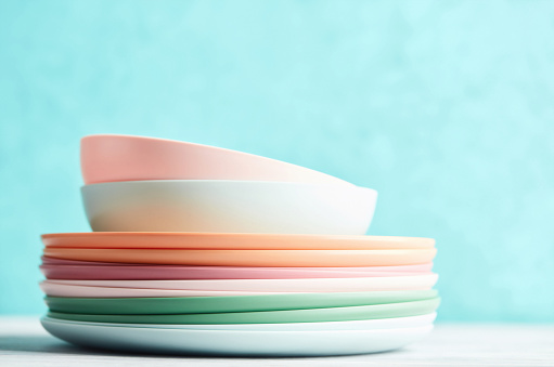 Collection of pastel colored plastic dishes in a bright setting. Reusable plates and bowls