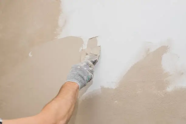 Man plastering wall with putty-knife. Fixing wall surface and preparation for painting.